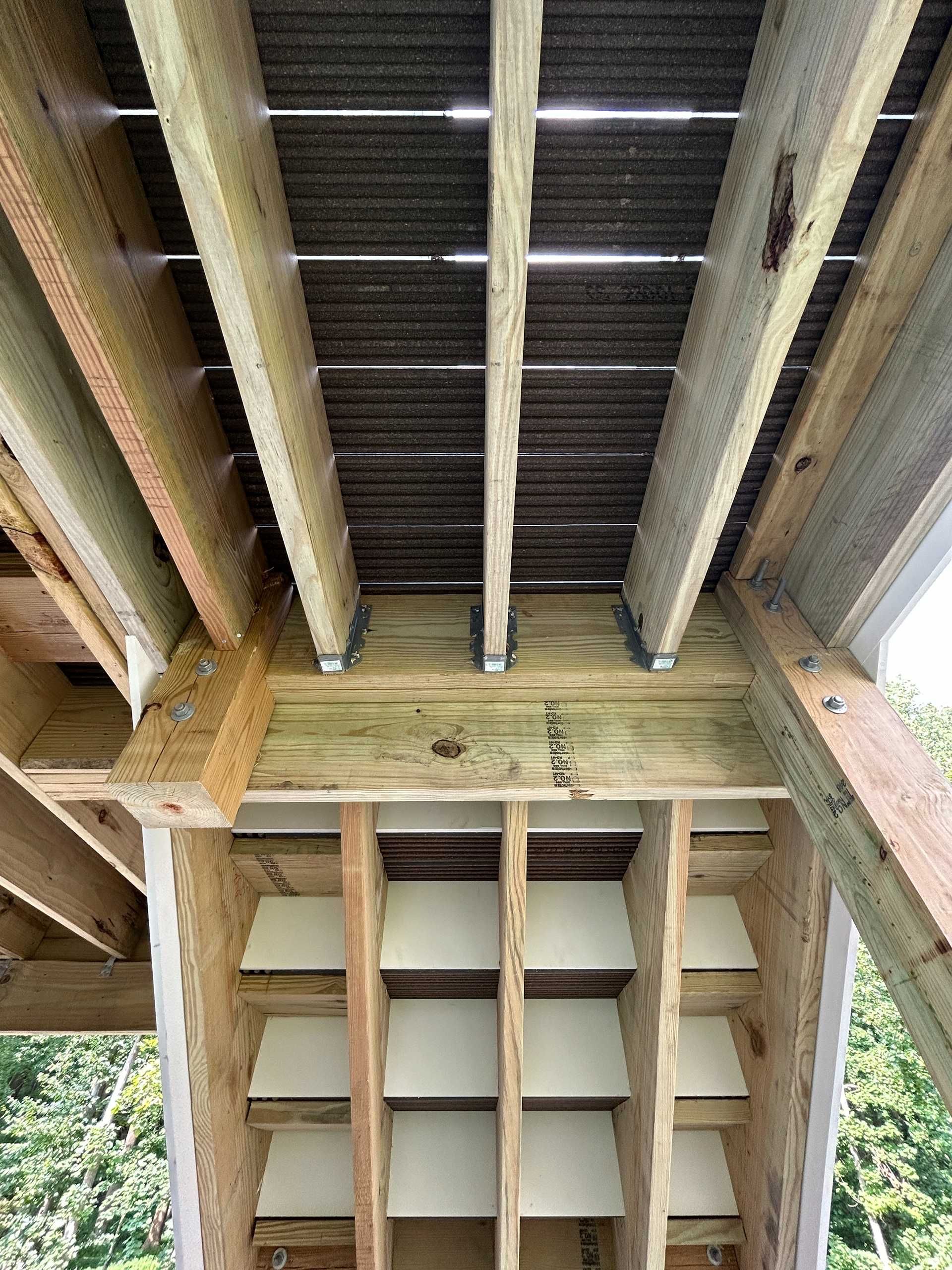 Underside view of wooden deck structure, with joists, beams, and insulation panels.