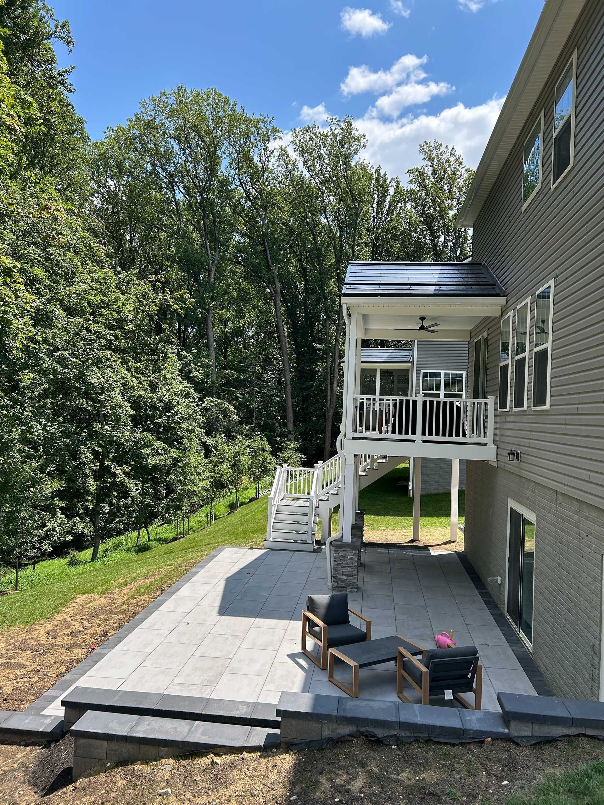 A home with a new stone patio and elevated porch overlooking a wooded area on a sunny day.