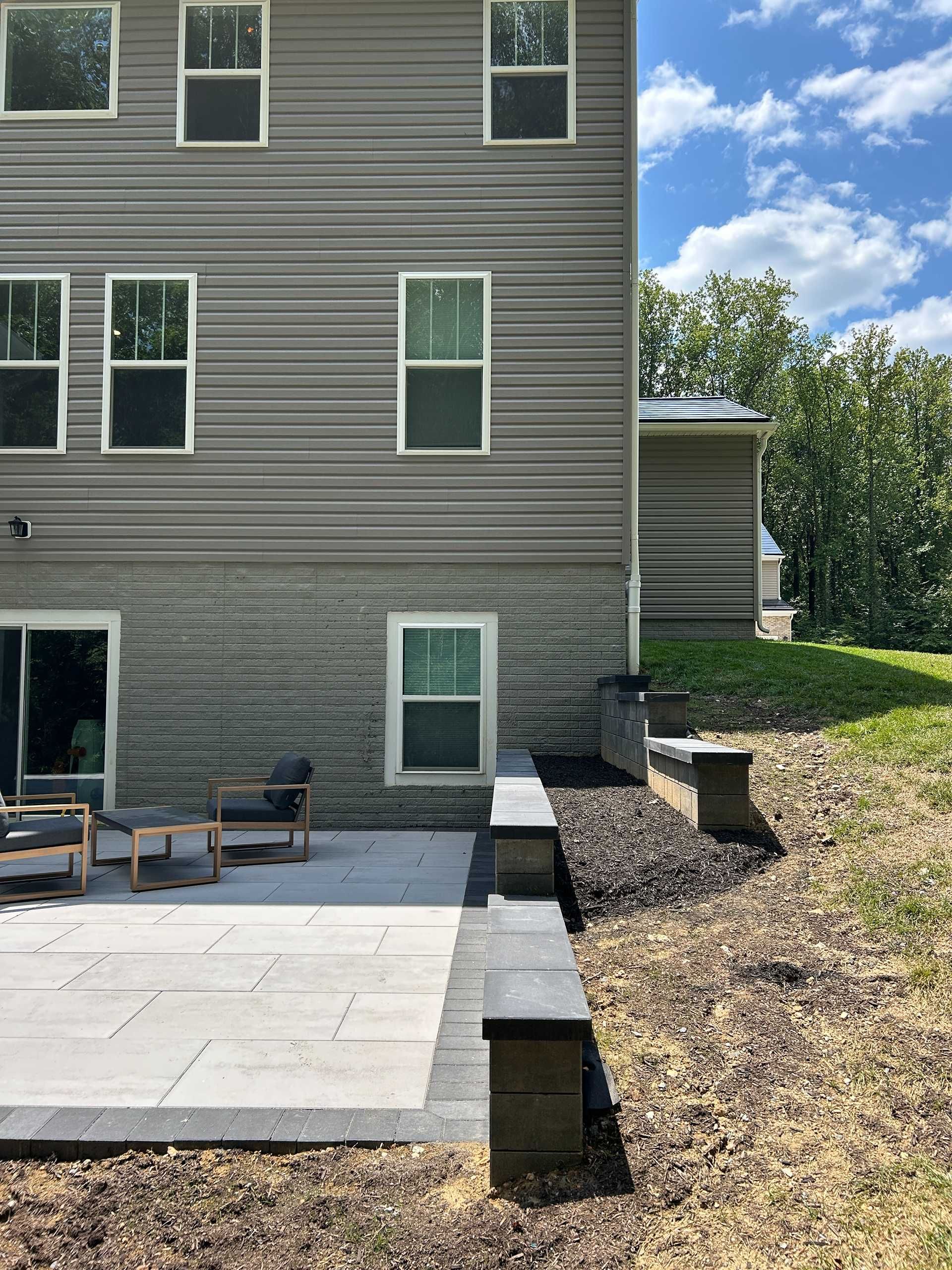 Gray house with multiple windows, patio, retaining wall, and green grass.