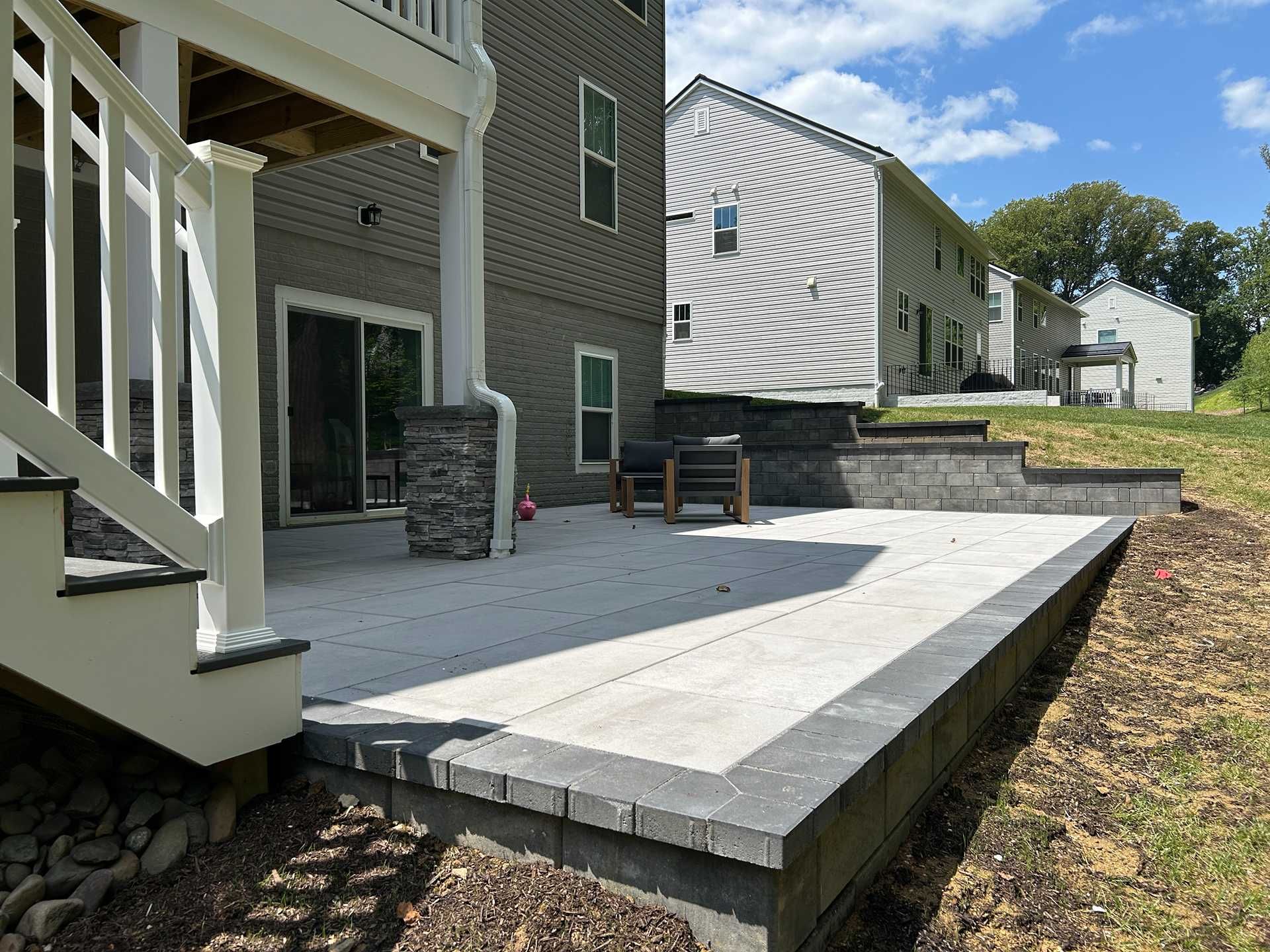 Backyard patio with gray brick pavers, retaining walls, and a house.