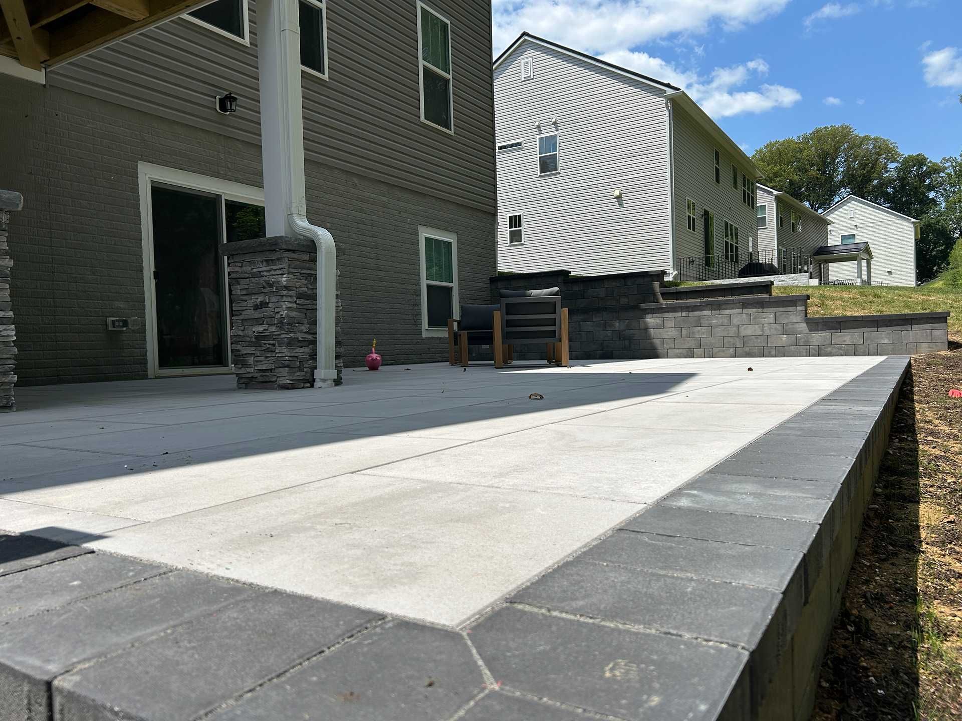 Concrete patio with dark border next to a house with stacked stone columns.