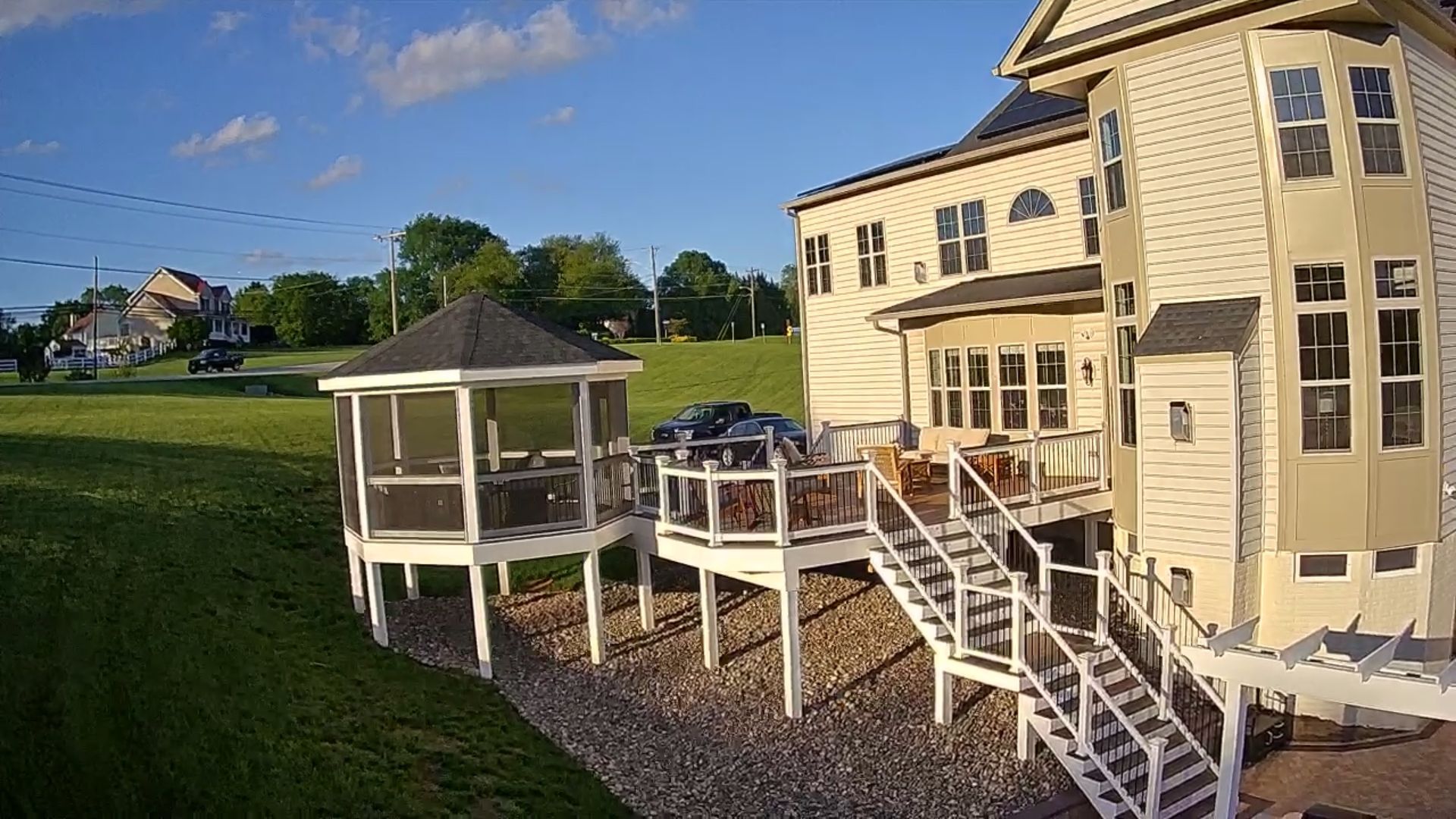 Two-story house with deck, gazebo on green lawn under blue sky.
