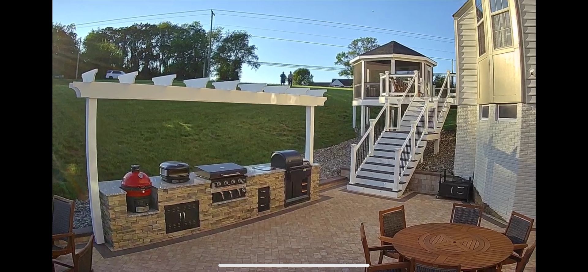 Backyard patio with outdoor kitchen, gazebo, and dining set. Person is using the grill.