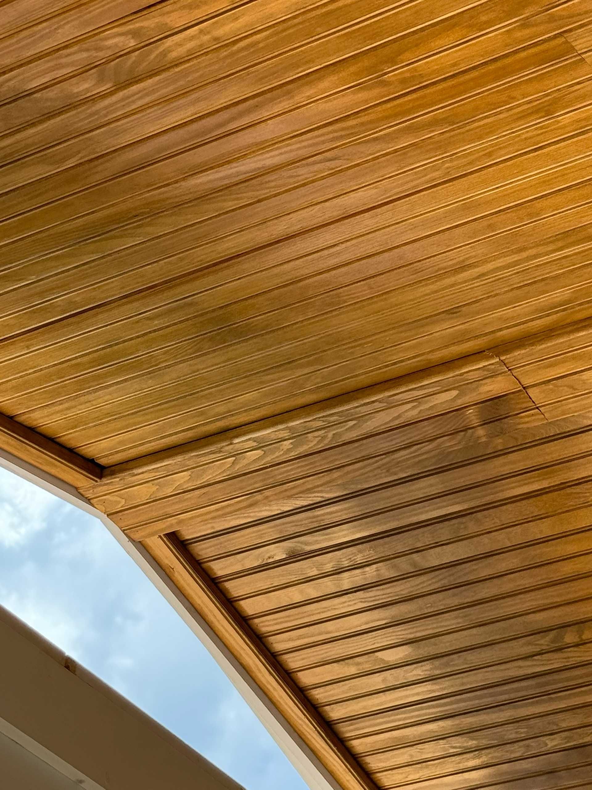 Wooden ceiling with horizontal planks, visible from below, against a blue sky.