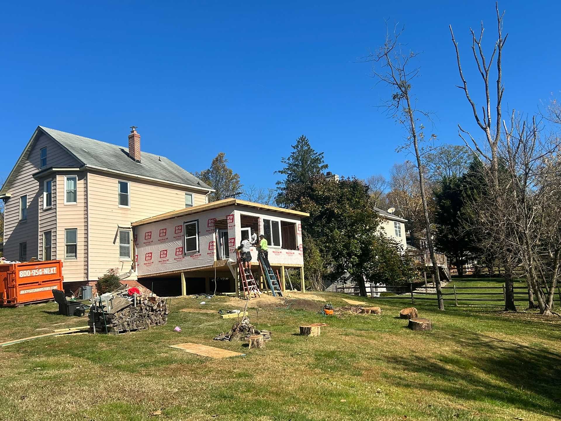 Construction workers building a porch addition onto a two-story house on a sunny day.