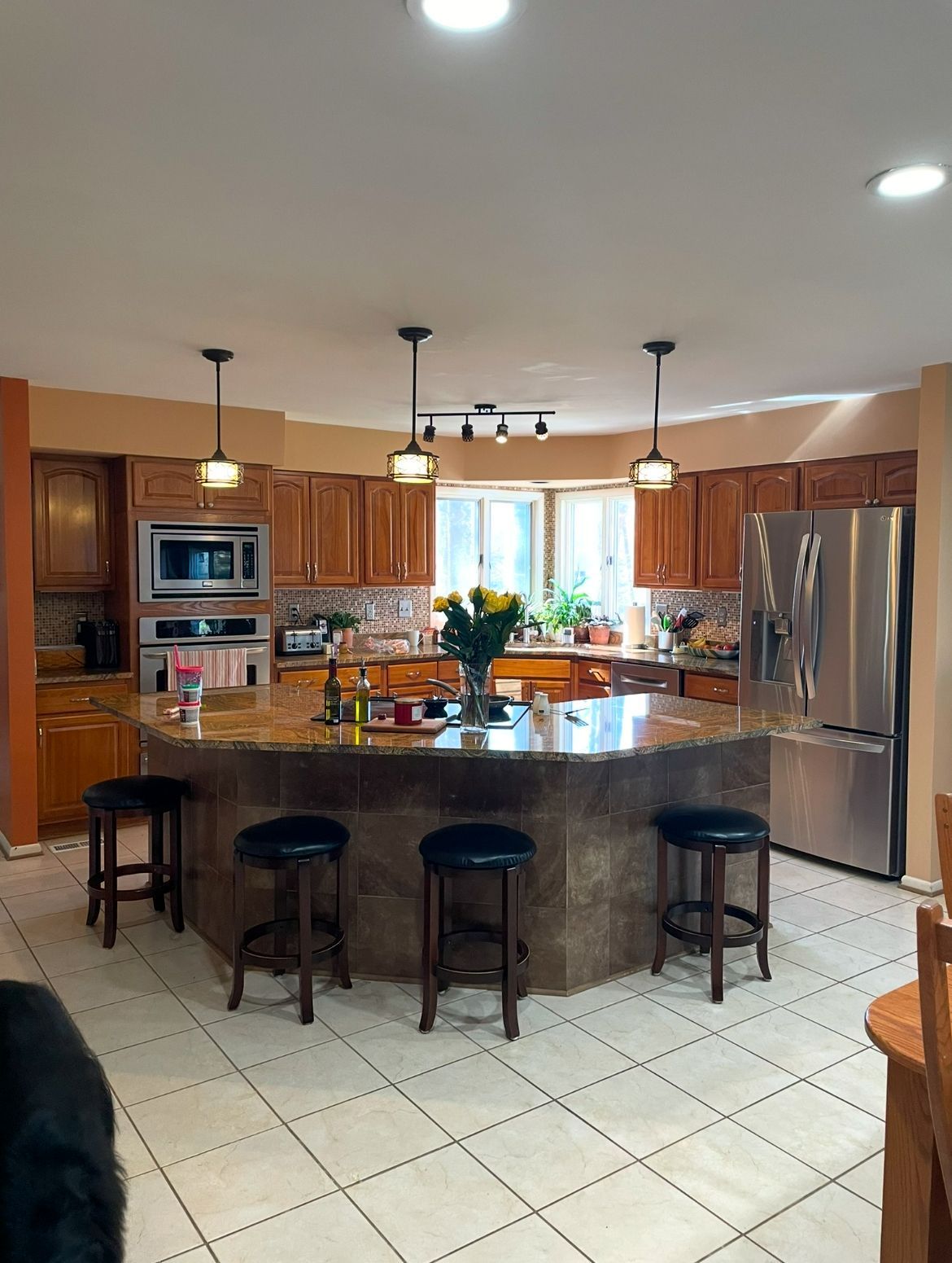 Kitchen with large granite island, wood cabinets, stainless steel appliances, and tile floor.