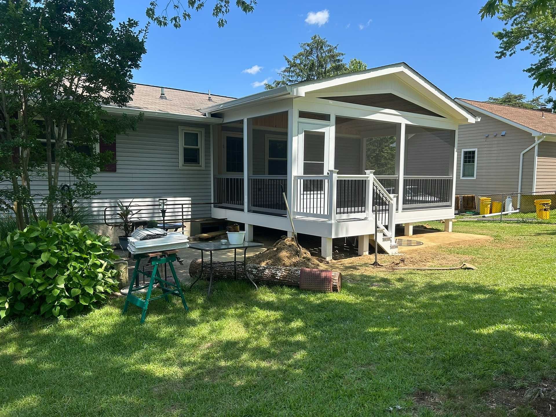 Backyard with a screened-in porch, grill, lawn, and adjacent house on a sunny day.