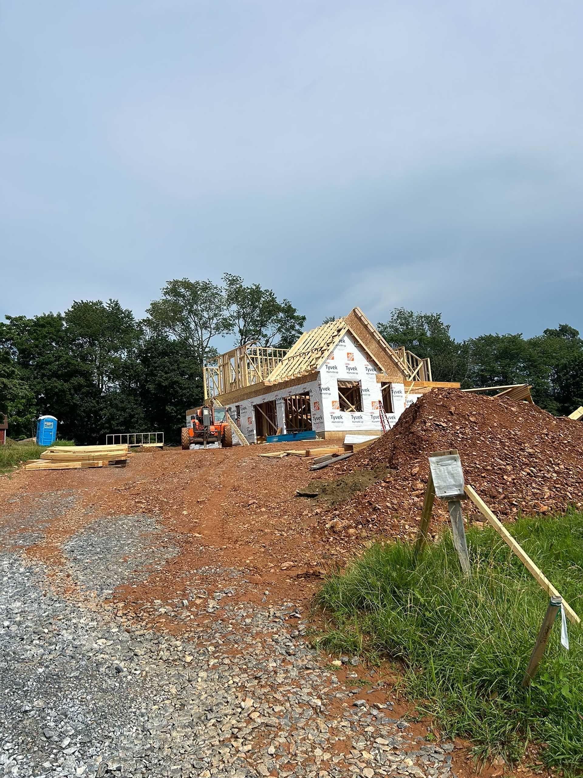 Construction of a house with exposed framing and roofing; dirt pile in foreground.