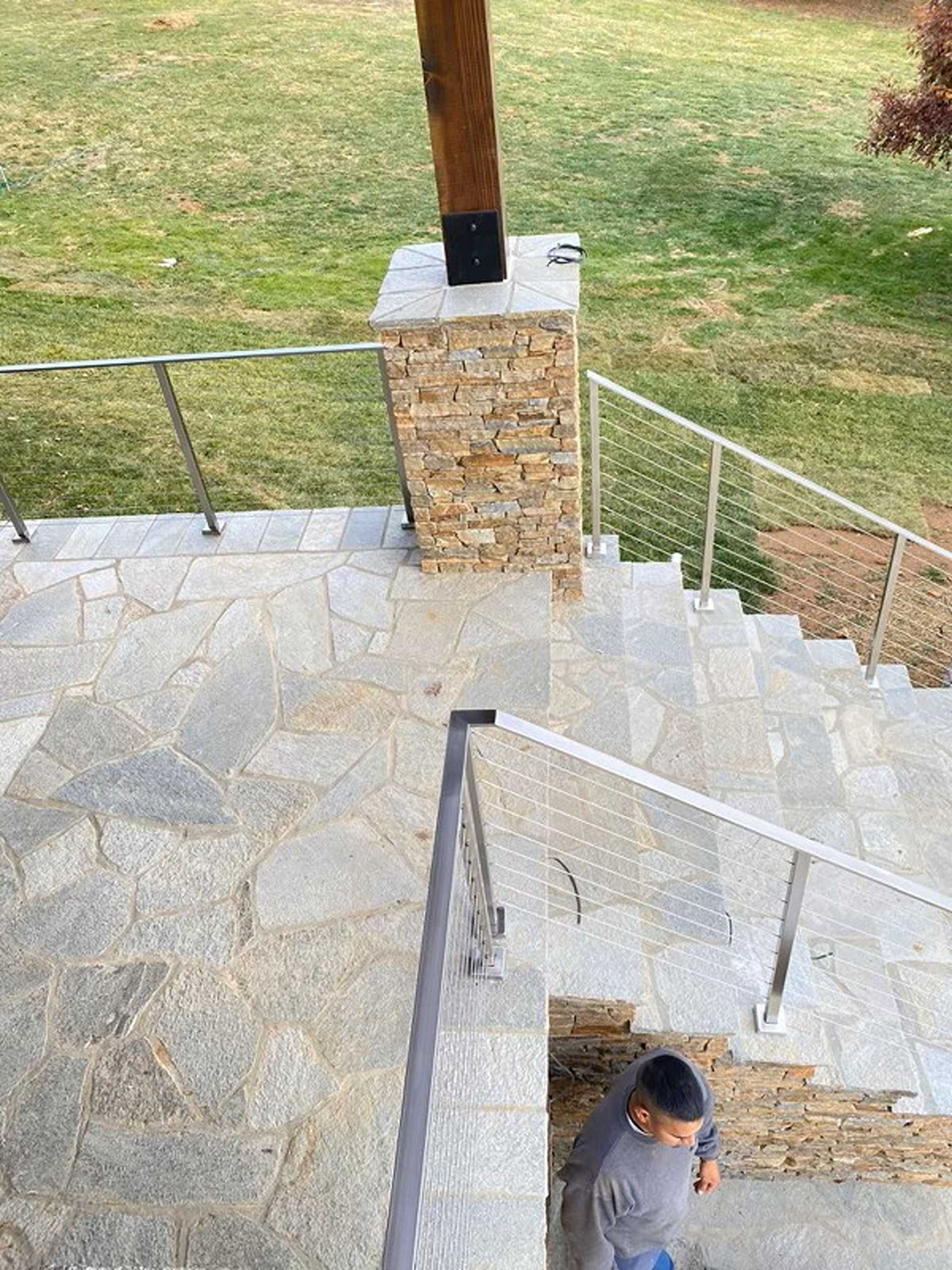Stone steps with metal handrails descend from a grassy area. A person stands at the bottom.