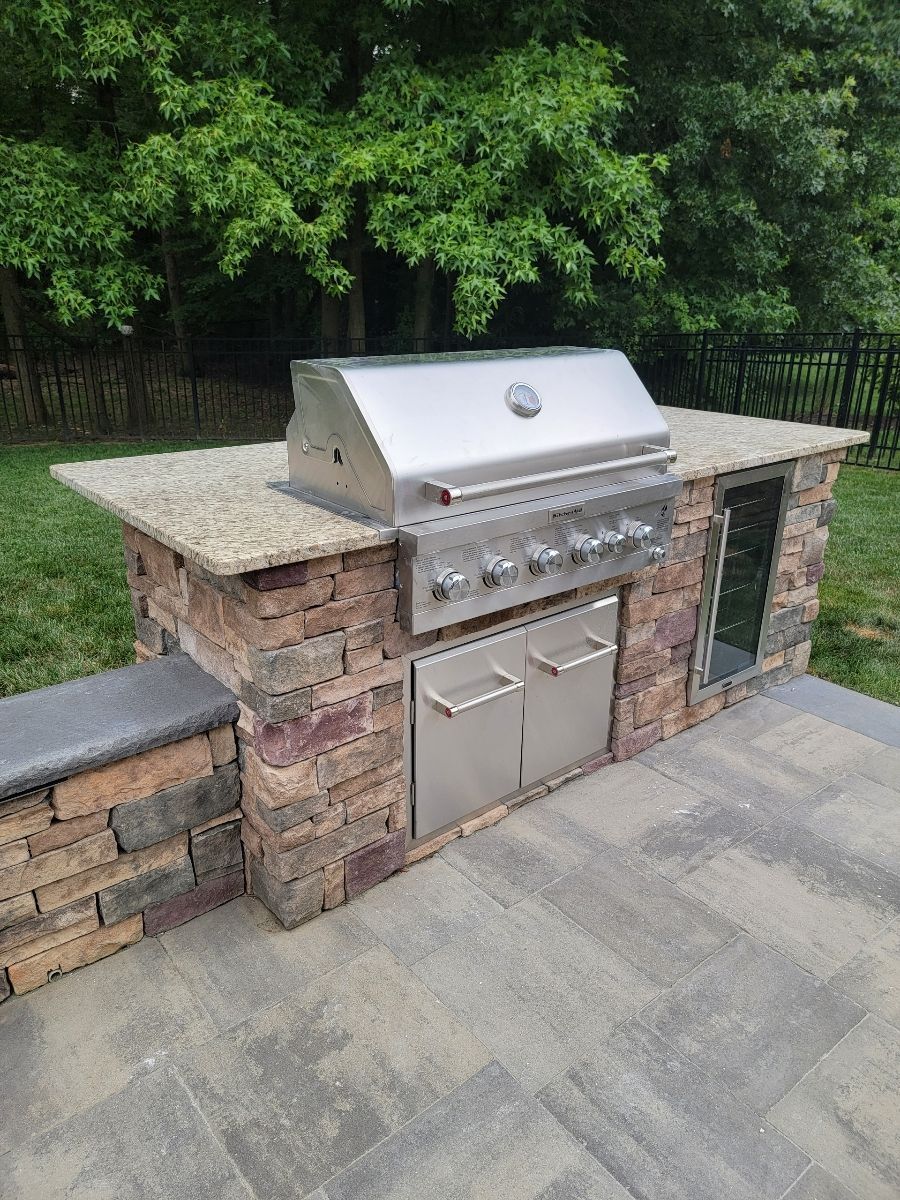 Outdoor kitchen with stainless steel grill, stone countertop, and brick facade on a patio.