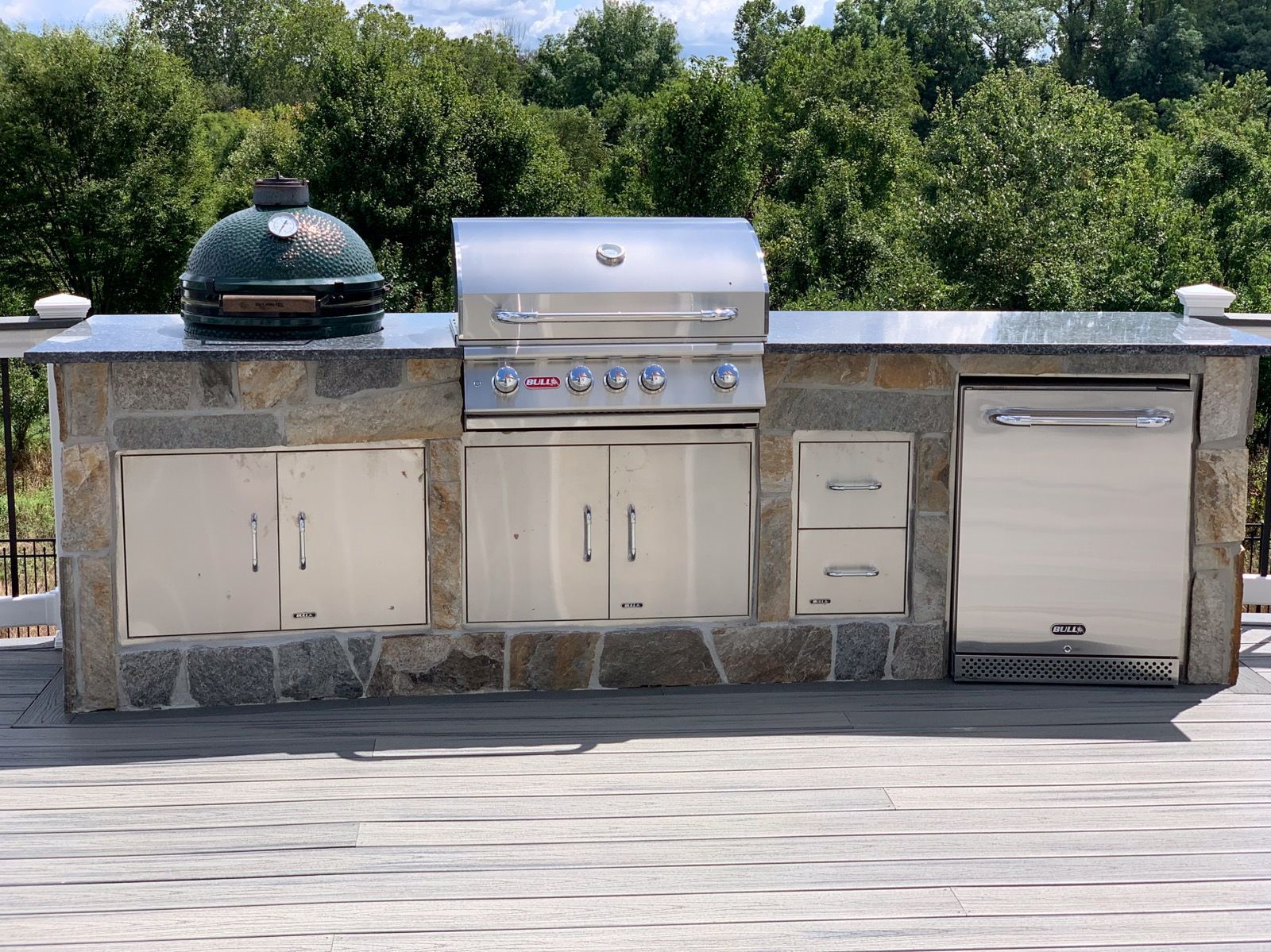 Outdoor kitchen with stainless steel grill, Big Green Egg, granite countertop, and stone facade.