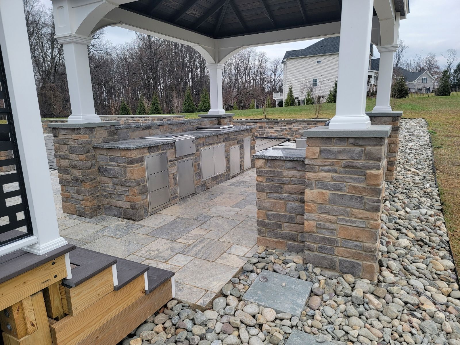 Outdoor kitchen with stone counters, under a white gazebo. Paver patio and stone border.