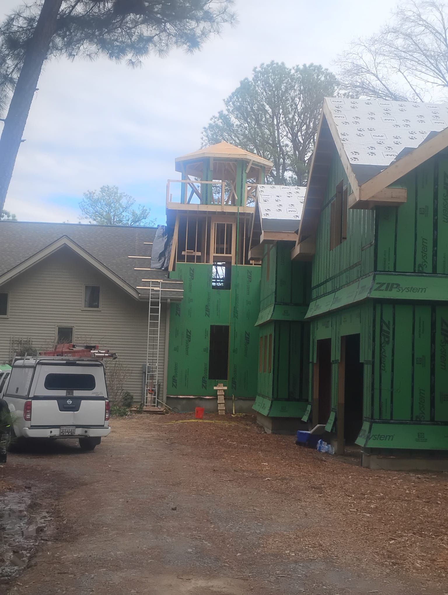 New construction house with unfinished wooden frame, green siding, and tower. A white truck parked in driveway.