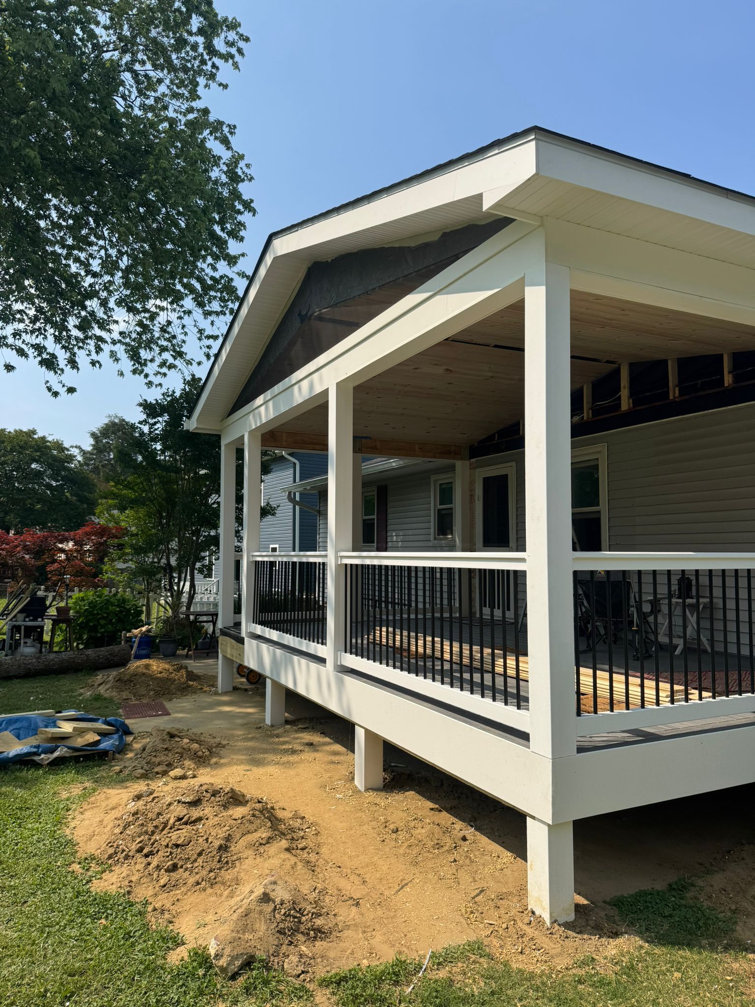 A newly built porch on a house with white trim, black railings, and a brown ceiling.