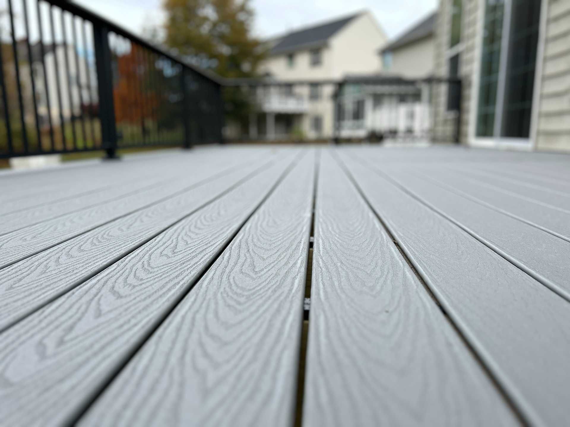 Close-up of a gray composite deck with house and railing in the background. Cloudy sky.