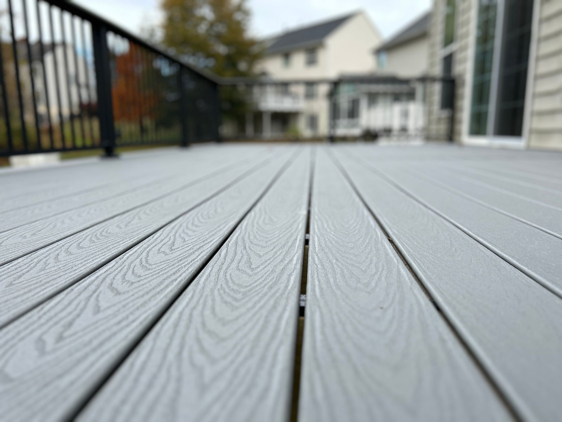 Gray composite deck with a black railing, blurred background of houses.