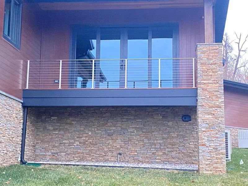 A two-story house with a stone facade deck and stainless steel railing.