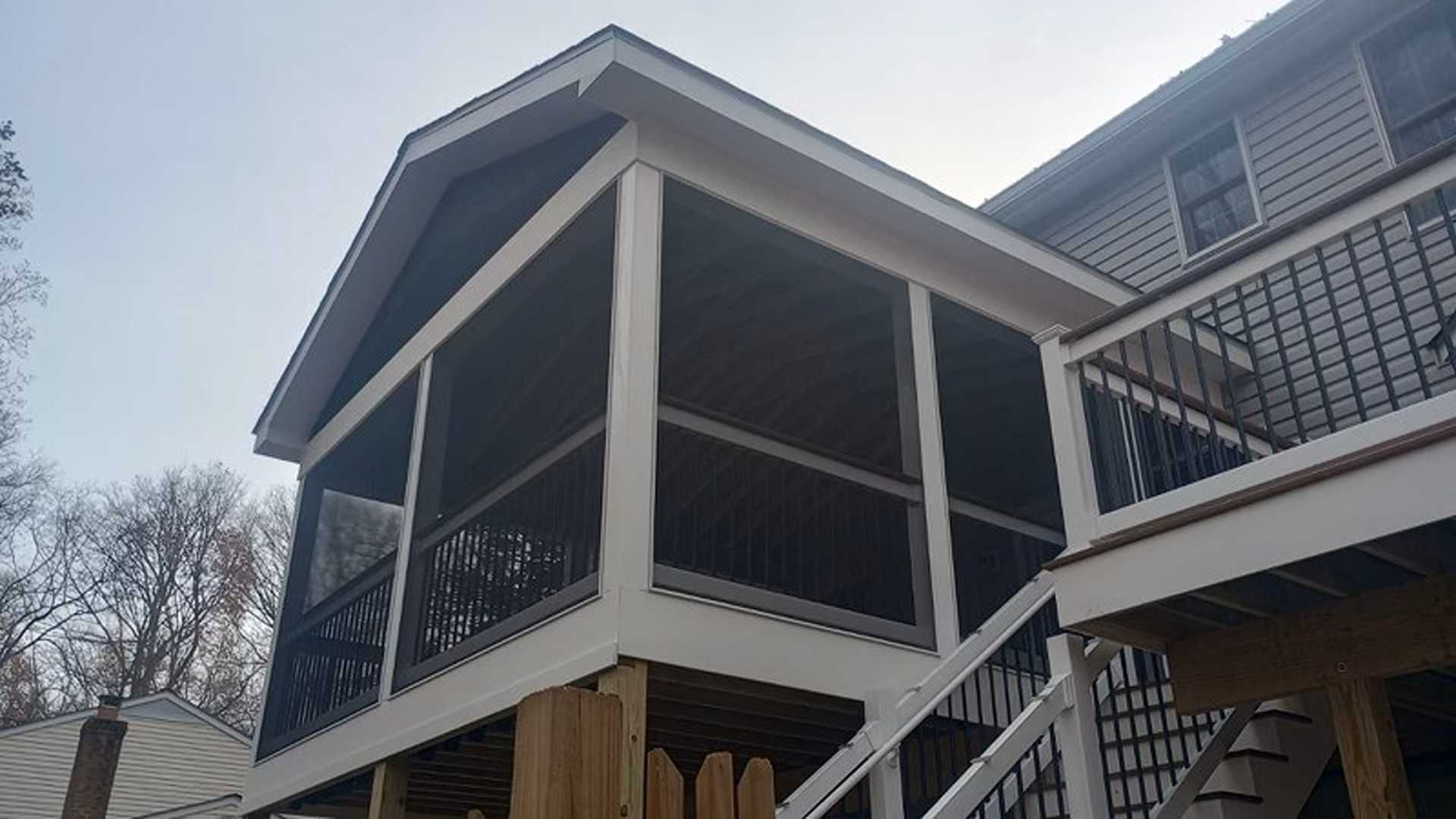 Screened porch addition on a house with a deck and stairs; white trim and dark screens.