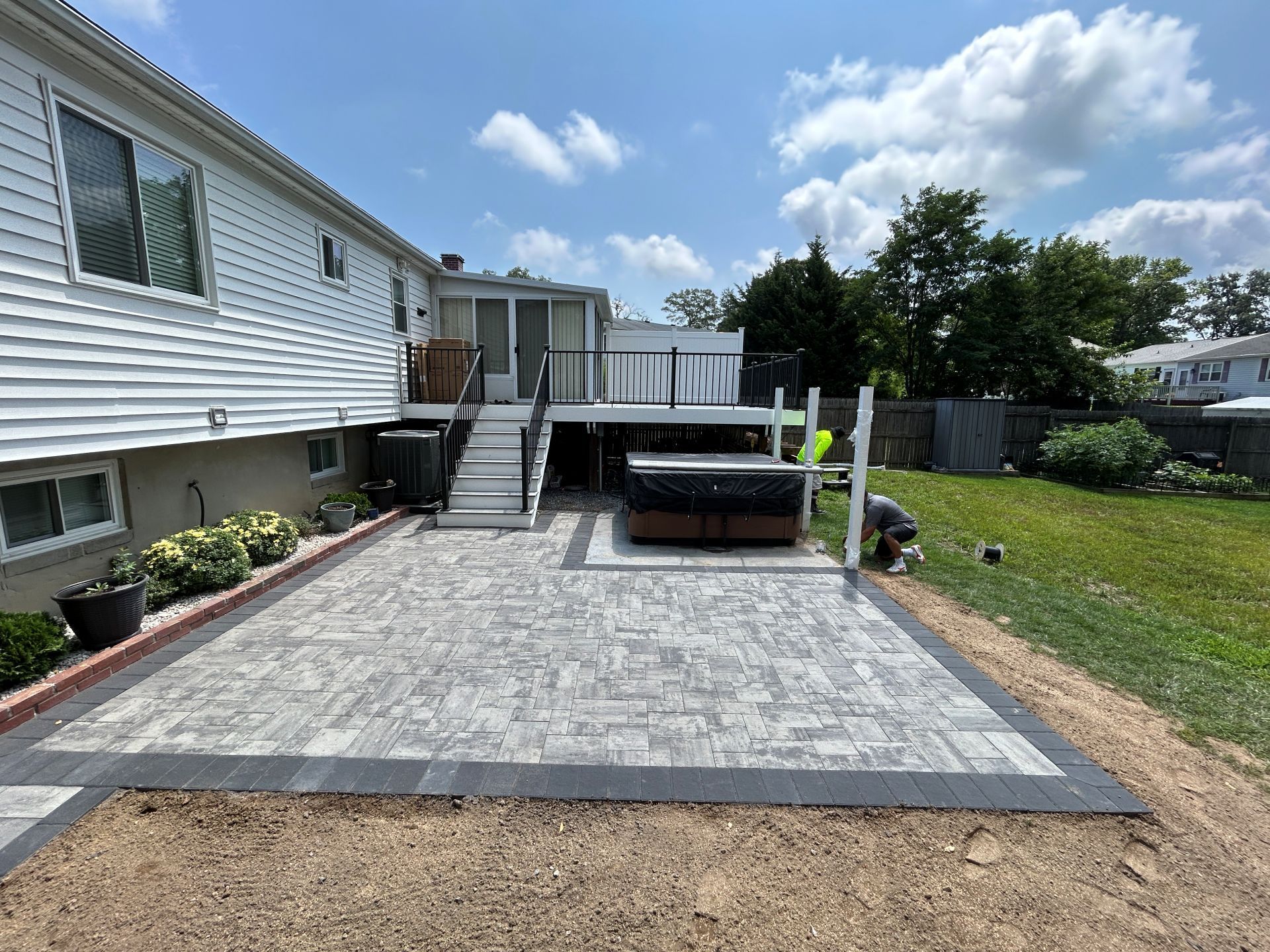 Backyard patio with hot tub, deck, and house under a blue sky.