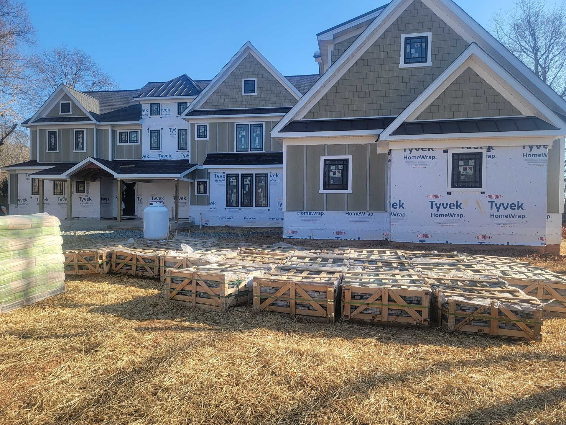Construction site with new multi-story house, siding partially installed, and crates of materials in the foreground.