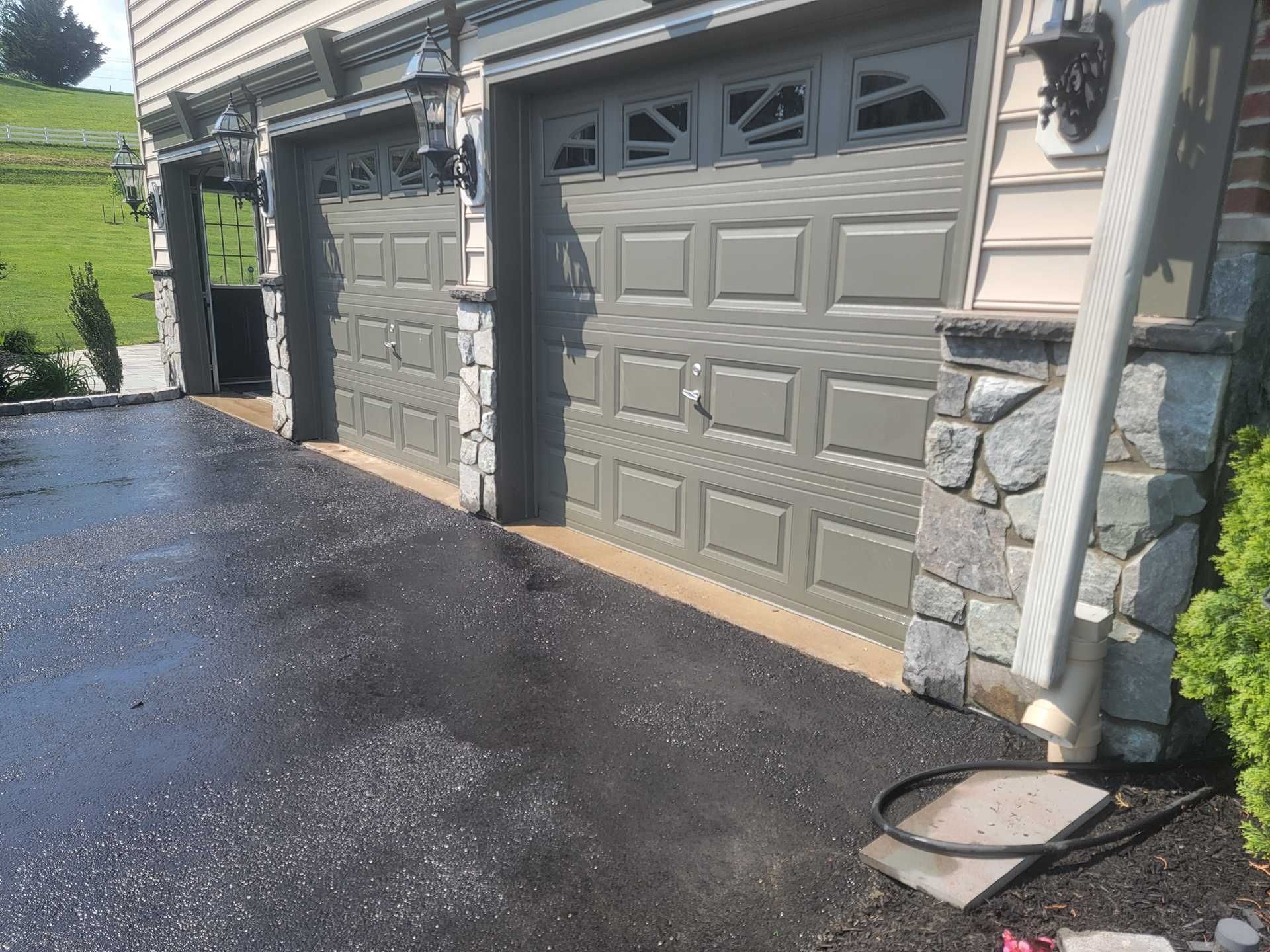 Three-car garage with gray doors, stone accents, and a wet asphalt driveway.