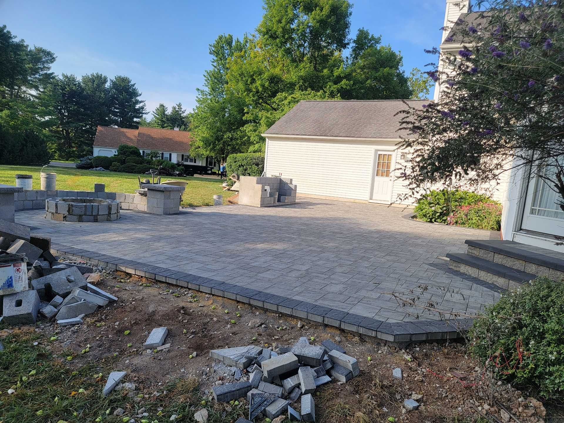 Patio with pavers, fire pit, small shed, and house. Concrete blocks are scattered in foreground.