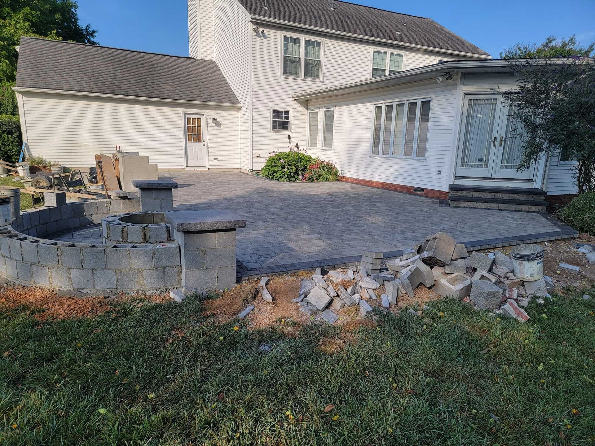 Backyard patio under construction with unfinished block walls and gray pavers. House in background.