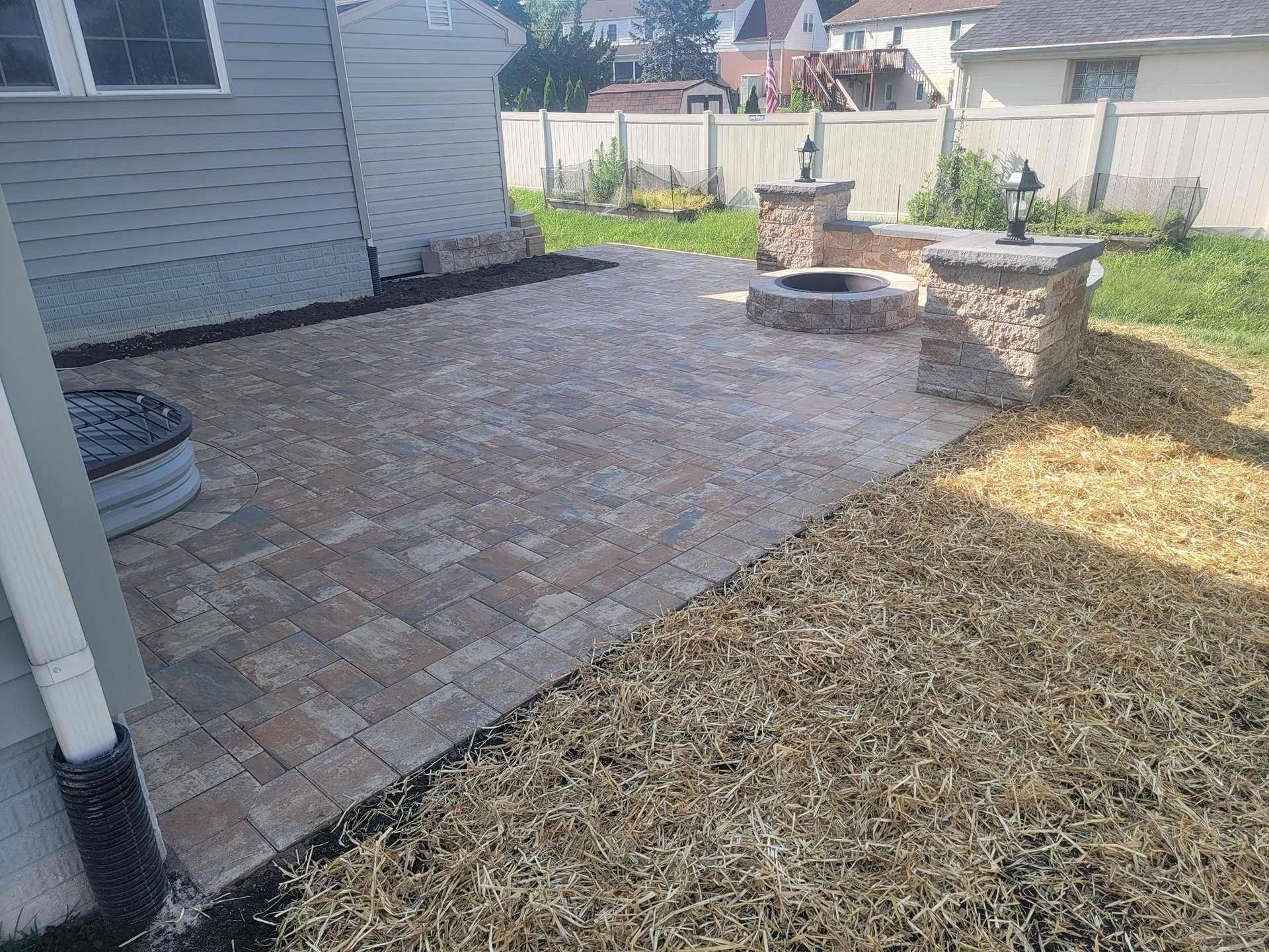 Patio with stone pavers, fire pit, and decorative columns in a backyard.