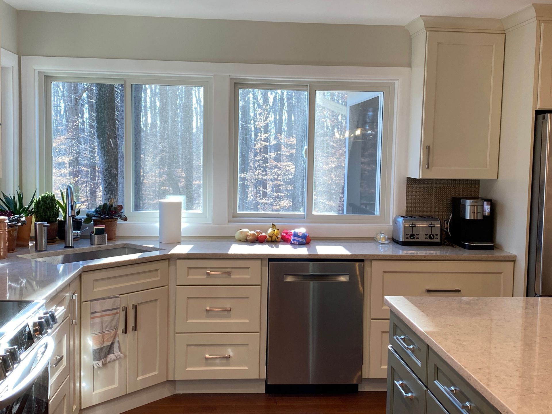 Kitchen with light-colored cabinets, stainless steel appliances, and a window overlooking trees.