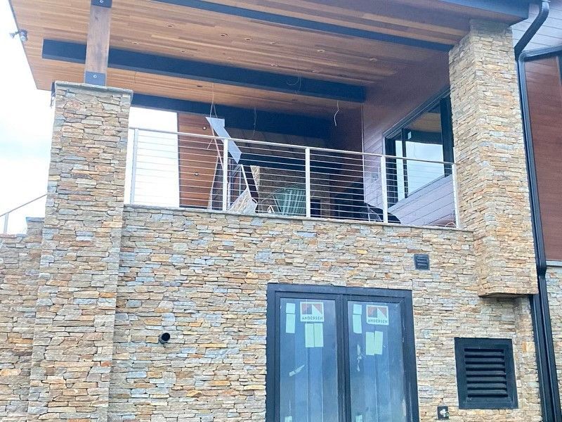 Stone facade with balcony and stainless steel railing. Wooden beams support the upper level.