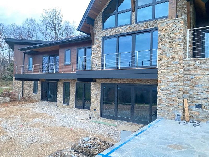 Multi-story house with stone facade, dark trim, and large windows.  Balconies with metal railings and dirt ground.