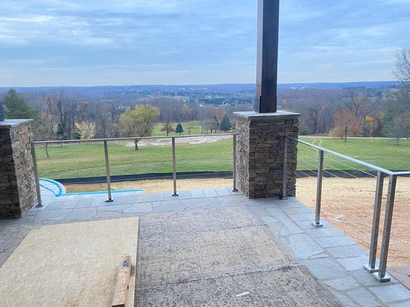 Patio overlooking a grassy field, with stone pillars, metal railings, and a cloudy sky.