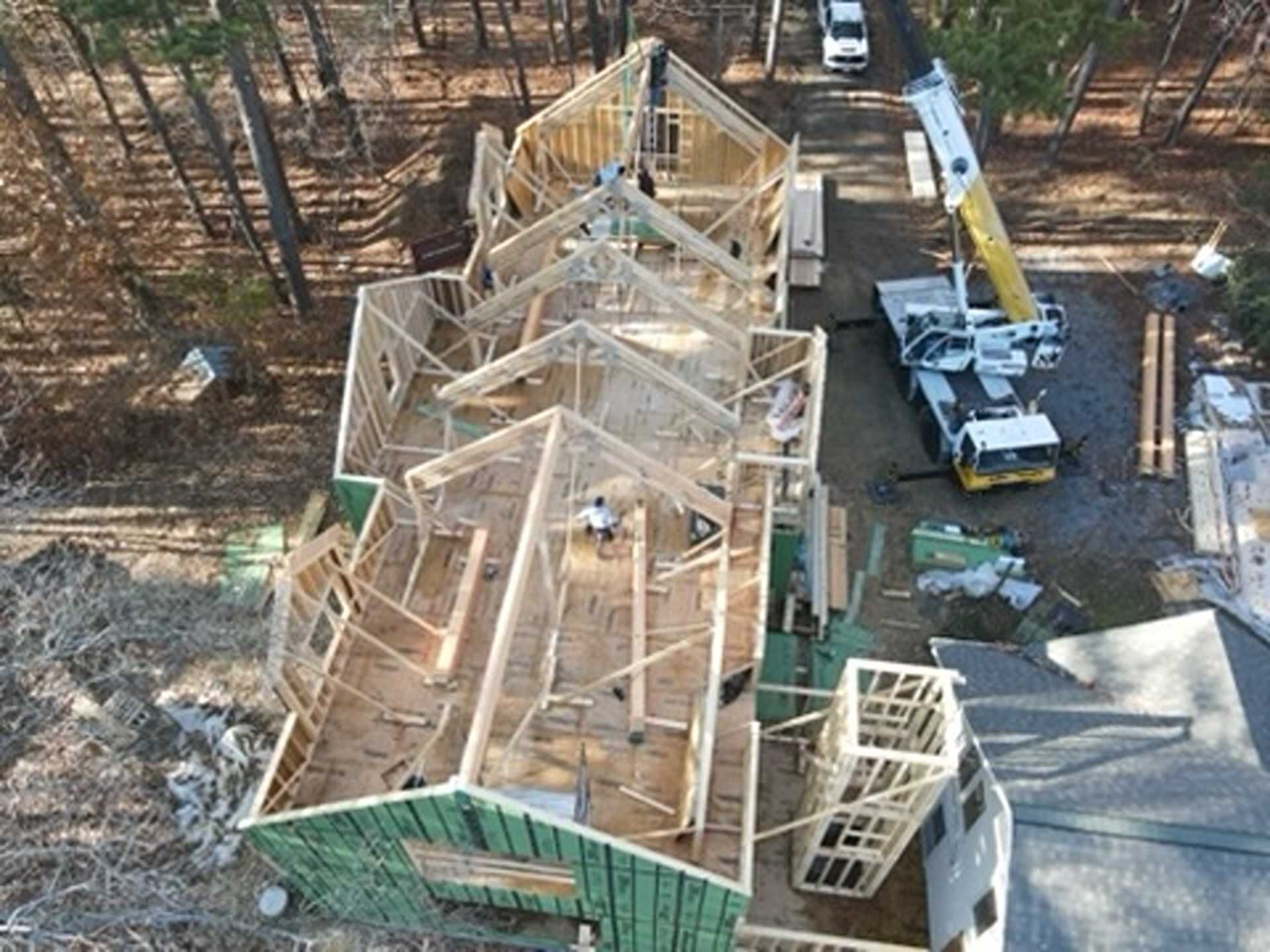 Construction site: Wooden framing of a house with a crane lifting materials; aerial view.