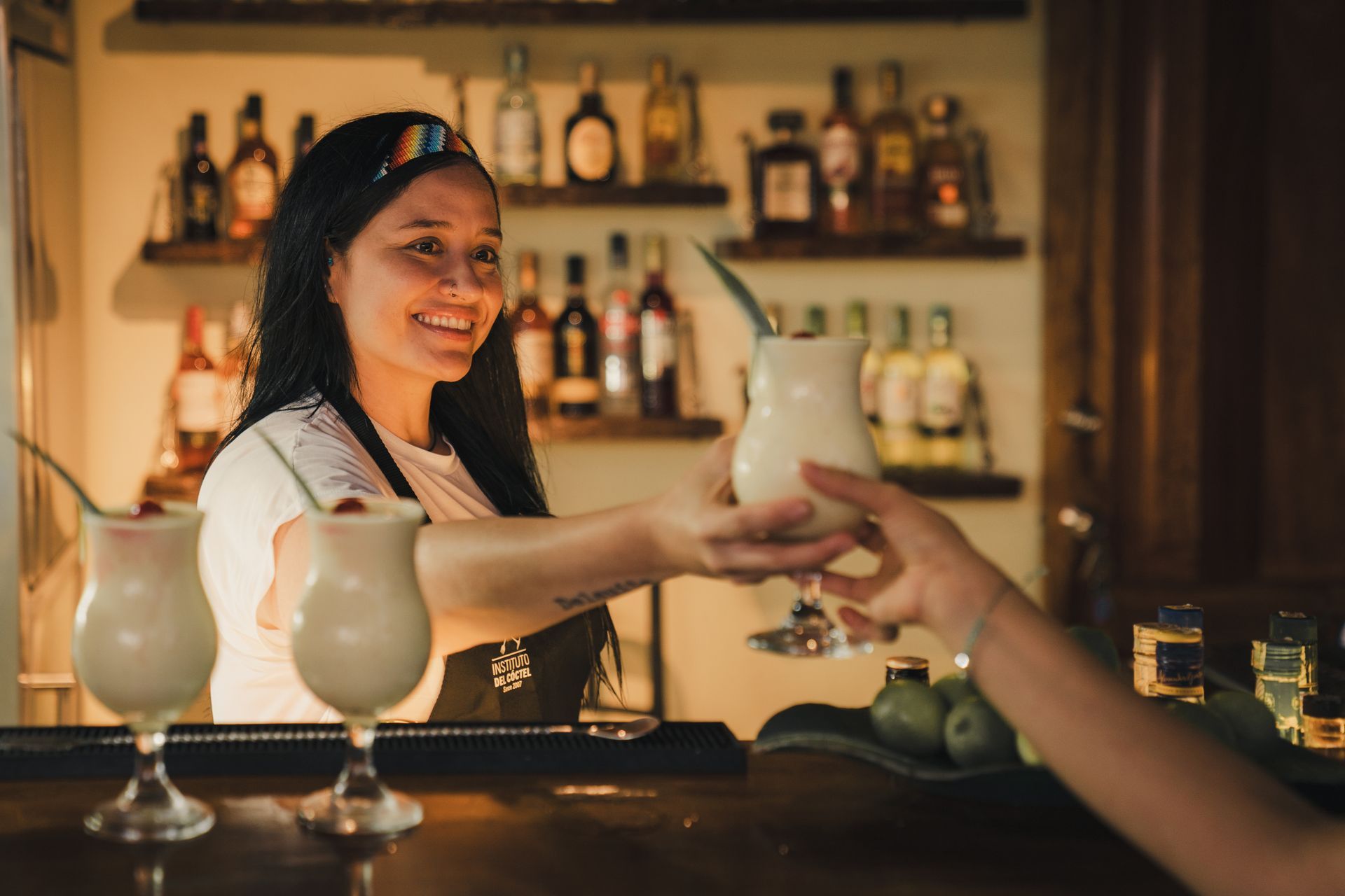 Bartender smiling and handing a cocktail to a customer at a warmly lit bar
