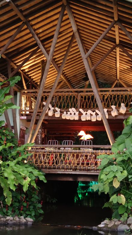 Thatched-roof open-air pavilion lit warmly at night, with lush green plants framing the entrance