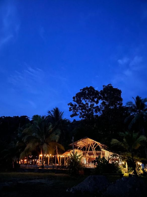 Tropical resort at dusk with lit huts and palm trees under a deep blue sky