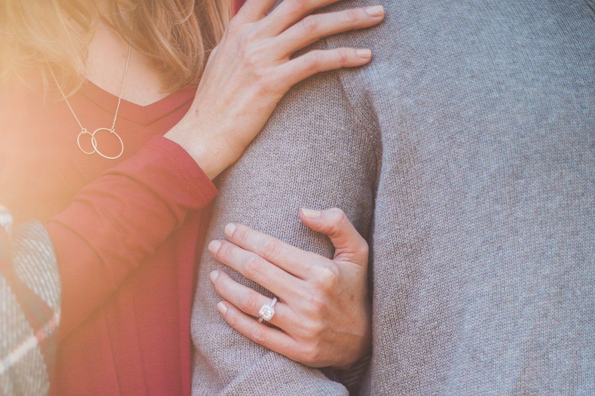 A woman wearing an engagement ring is hugging a man.