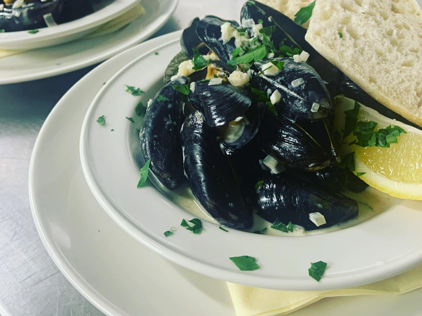 white dishes stacked with mussels in broth lemon and parsley and bread
