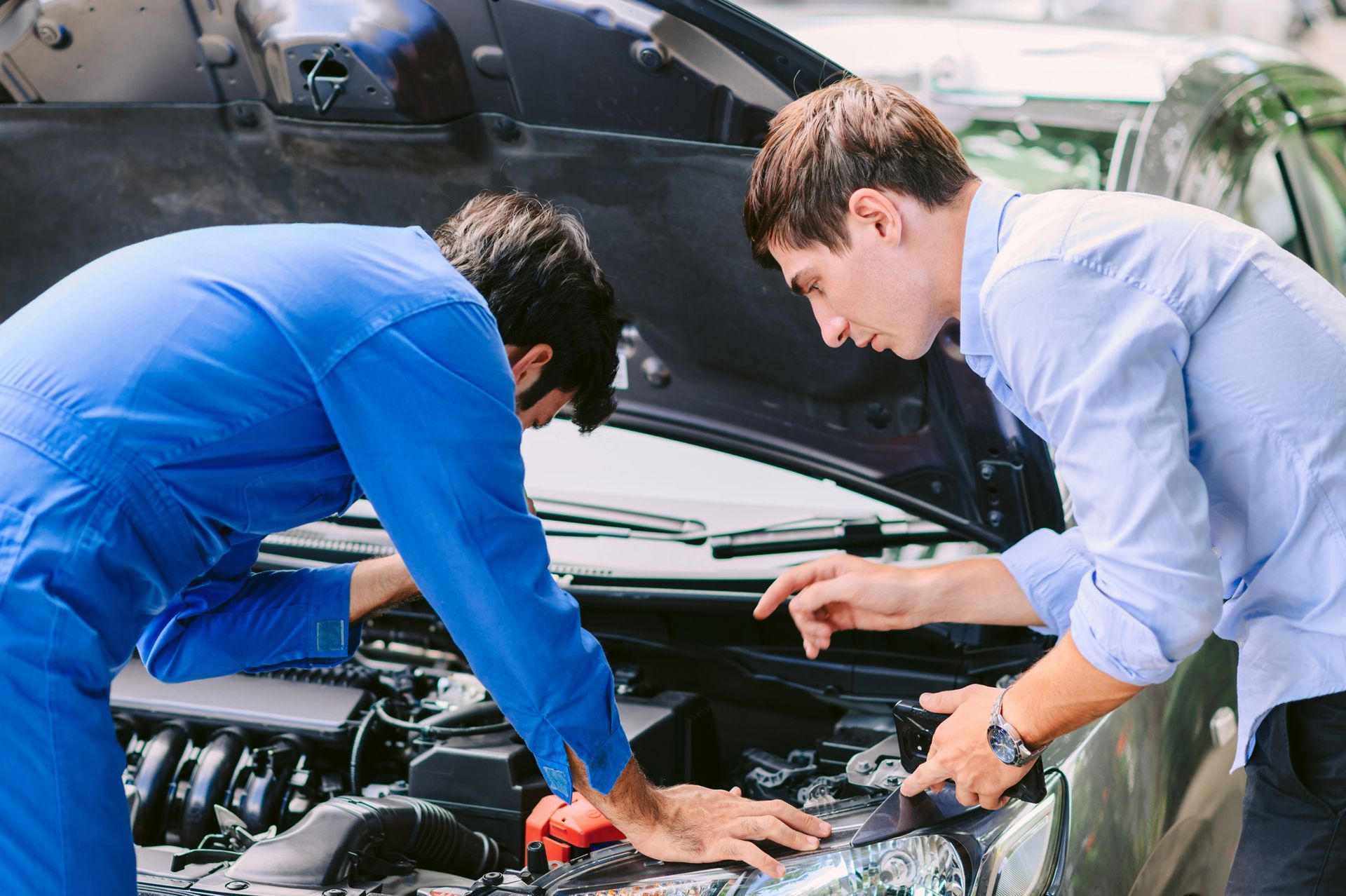 Two men are working on the engine of a car.