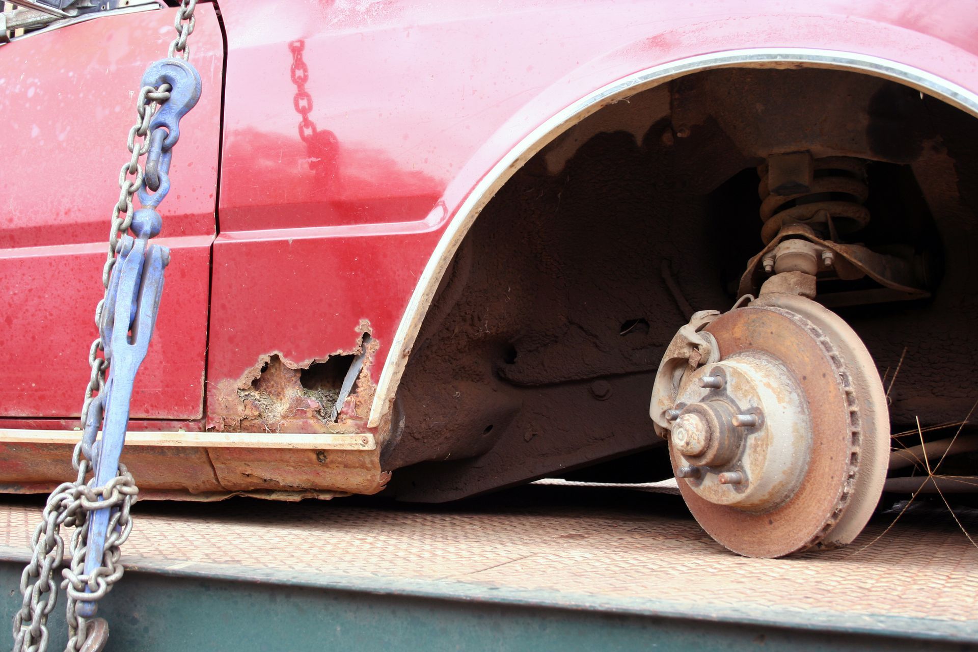A red car with a broken wheel is being towed by a chain.