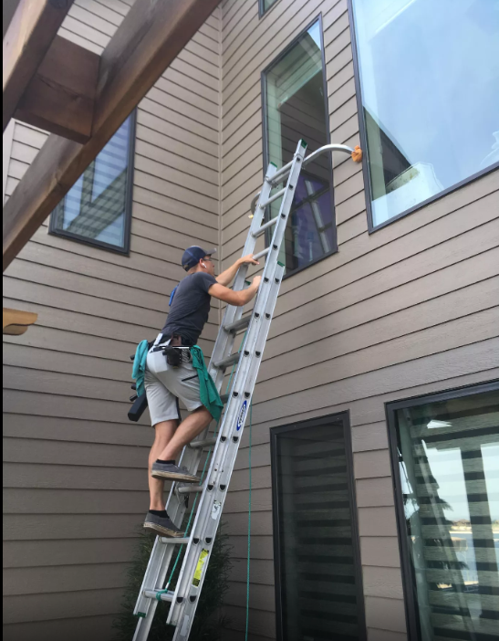 A man is standing on a ladder cleaning a window.