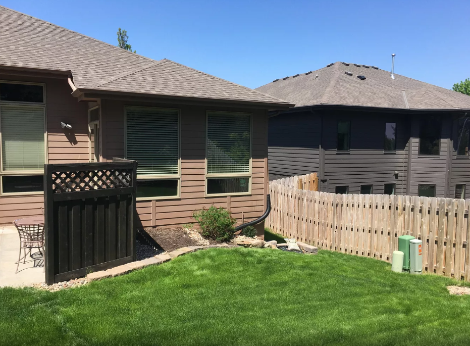 A backyard with a wooden fence and a house in the background.