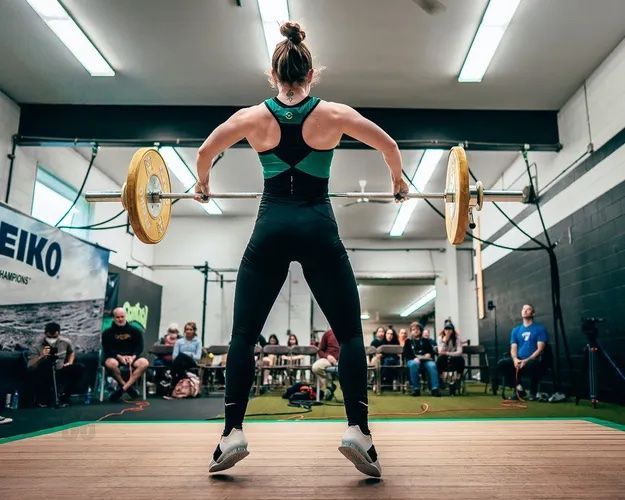 Female weightlifter in black and green lifting barbell, audience watching.