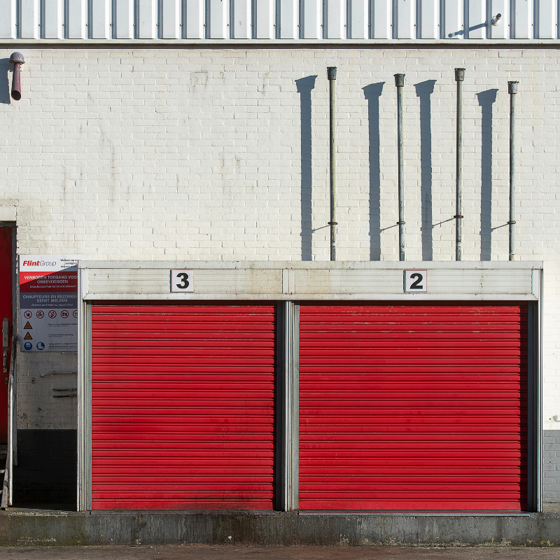 Red storage unit doors with numbers 2 and 3 on them against a white brick wall.