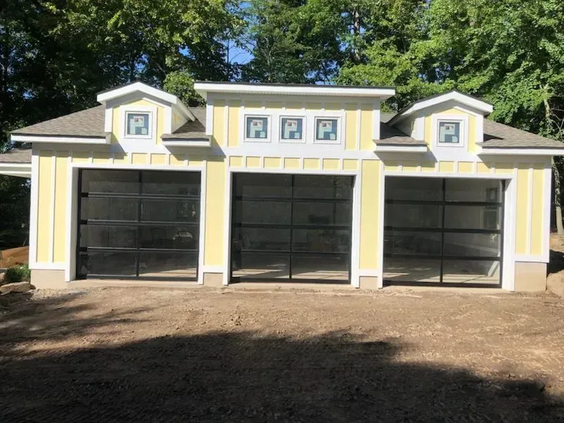 Yellow three-bay garage with black glass doors, windows, and light tan trim; set in a yard.