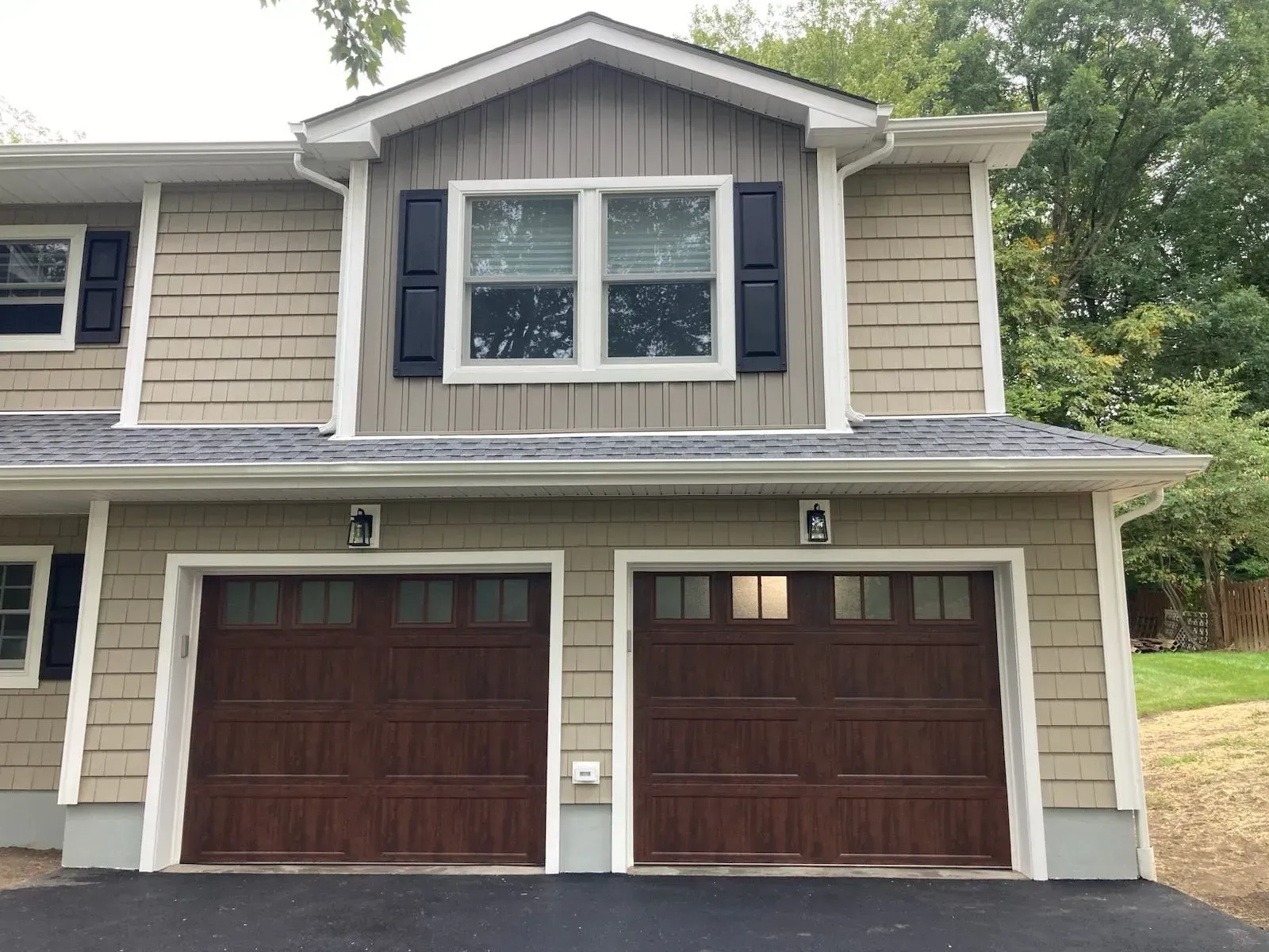 Two-story house with brown garage doors and matching siding. Top section has windows and dark shutters.
