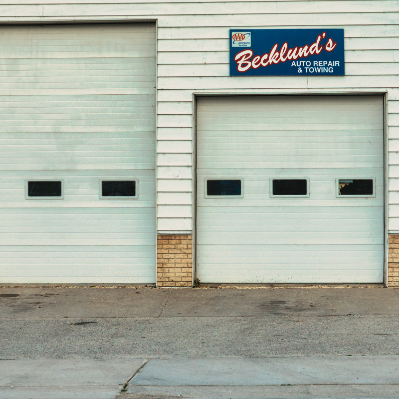 White garage doors of Becklund's Auto Repair & Towing, with a blue and red sign, set against a grey concrete surface.