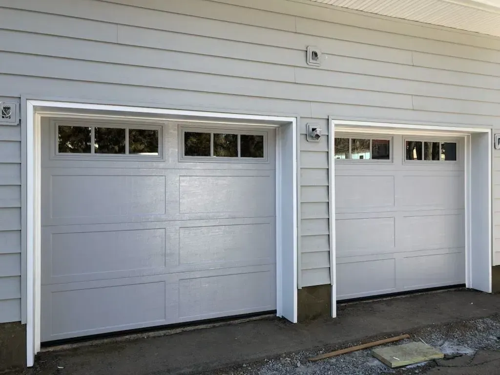 Two white garage doors with windows, in a light gray house.