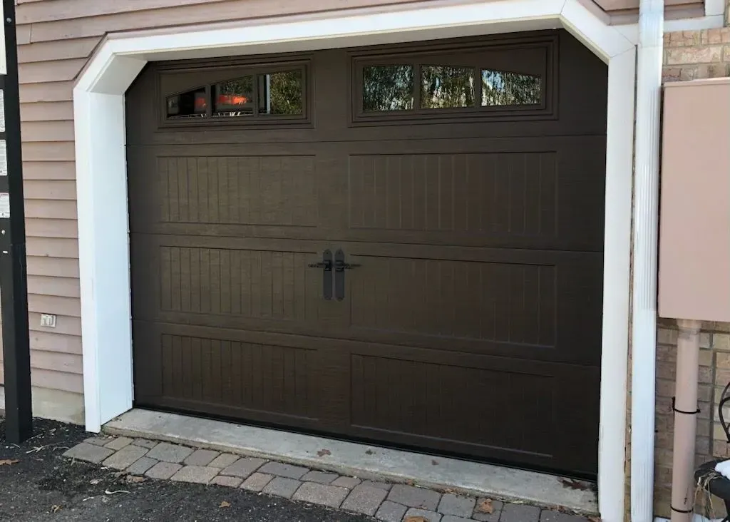 Brown garage door with windows, handles, and white trim.