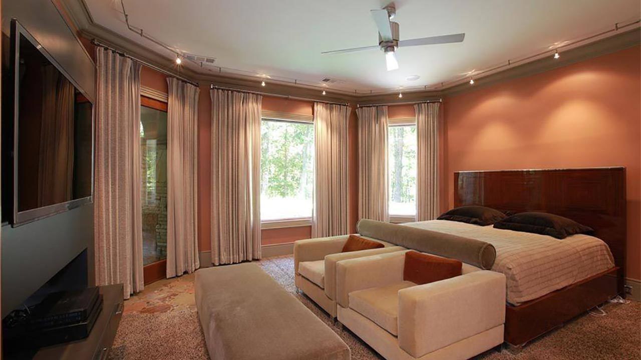 A bedroom with a large bed , two chairs , a television and a ceiling fan.